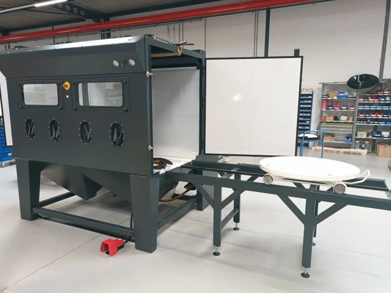 Tryskací kabina se s otočným stolem na kolejnicové trati a úpravou střechy pro zavěšení obrobku na jeřáb